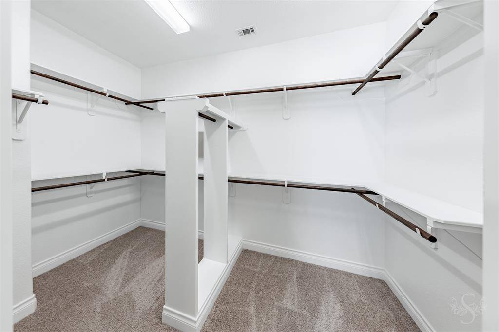A boutique-style walk-in closet offers abundant storage with a custom built-in, double-tier hanging rods, shelves and plush carpeting. Thoughtfully designed to keep everything organized and accessible.