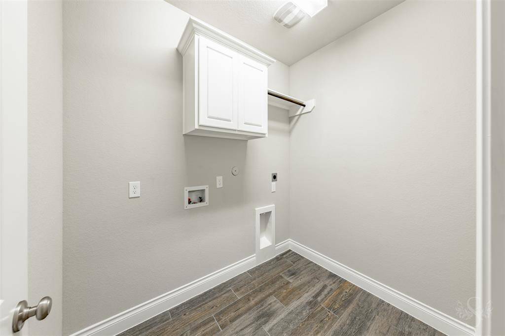 This spacious utility room includes upper cabinetry, hanging space, and durable tile flooring. With room for full-size appliances and extra storage, it blends practicality with clean design.