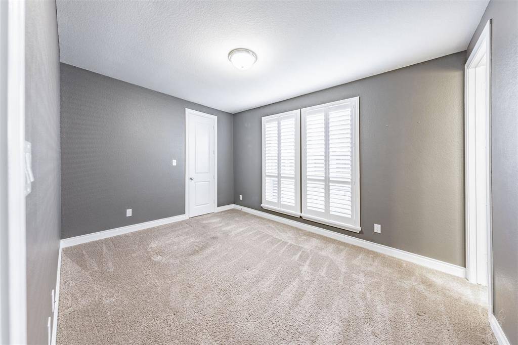 This spacious secondary bedroom on the main floor features windows with plantation shutters, plush carpeting, and soft natural light. Ideal for guests or multi-generational living, it offers both privacy and comfort with direct access to a full bath.