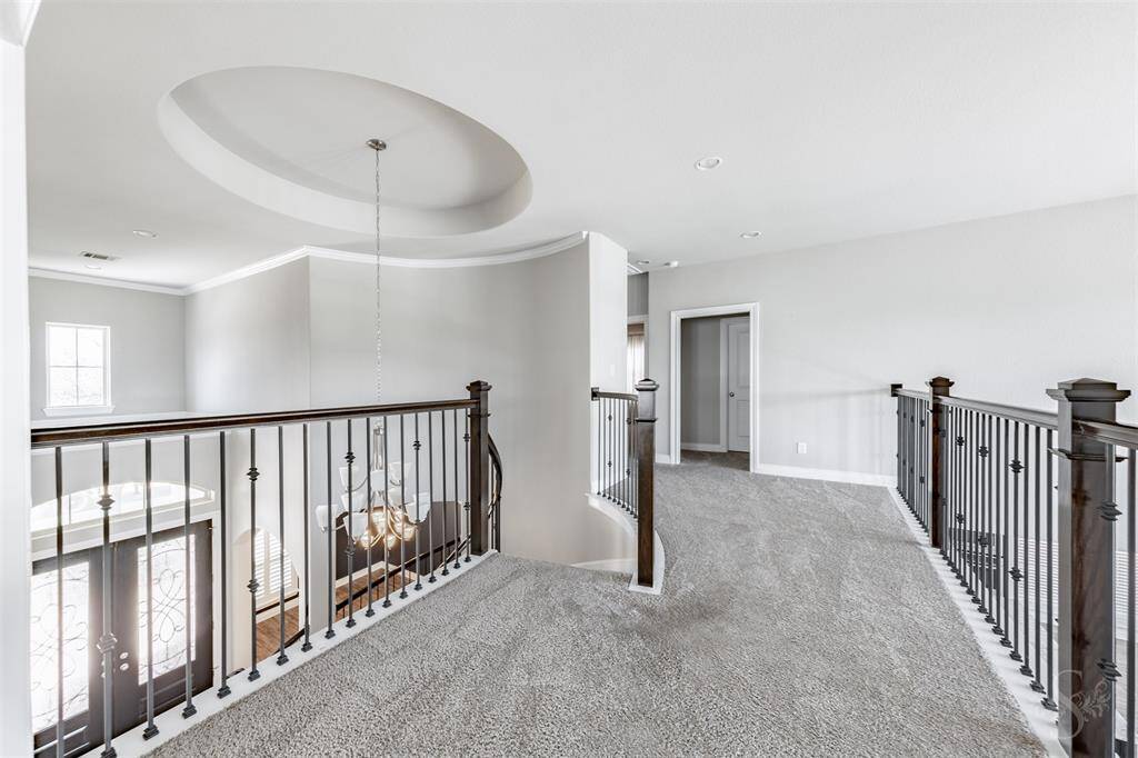 The upstairs landing showcases decorative wrought iron railings, crown molding, and views of the grand entry and 2 story family room below. With open sightlines and architectural detail, this space adds an airy elegance to the second level.