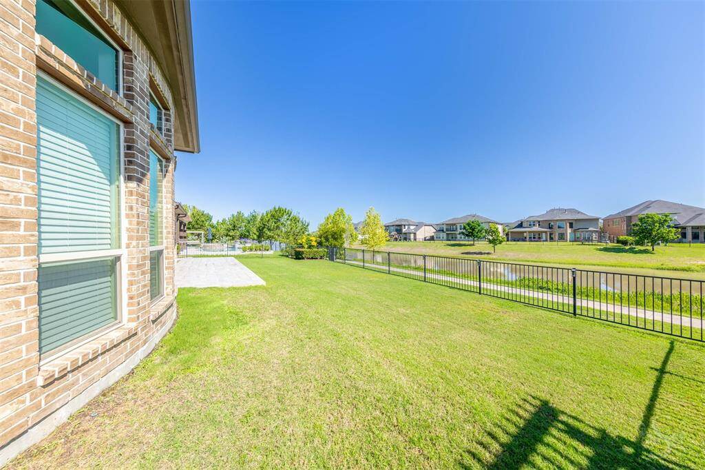 A spacious yard offers lush green lawn bordered by wrought iron fencing, giving way to uninterrupted water views. The wide-open layout invites possibilities for a pool, garden, or simply enjoying the open space.