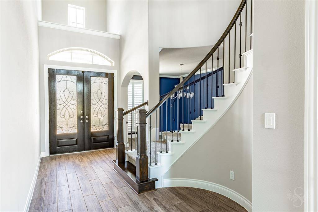 Step through the elegant wrought iron detailed double doors into a soaring 2 story entryway highlighted by a sweeping staircase with wrought-iron balusters. Beautiful light-colored wood-look tile flooring and designer touches throughout create a timeless first impression.