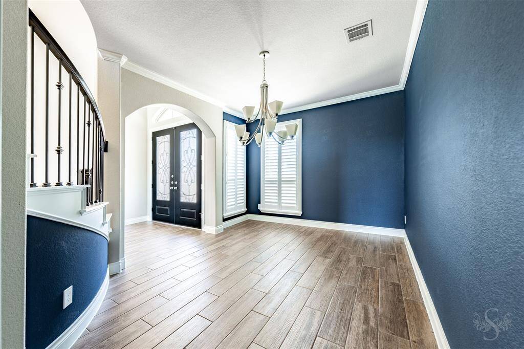 This inviting formal dining room features crisp white crown molding, a lovely chandelier, and window with plantation shutters for timeless charm. Arched entryways and elegant flooring add to the home’s refined aesthetic.