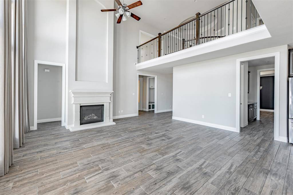 A view of the spacious family room highlights the soaring ceiling, modern gas fireplace, and open sightlines throughout the main living areas. Crisp, neutral tones and natural light enhance the luxurious yet livable atmosphere.