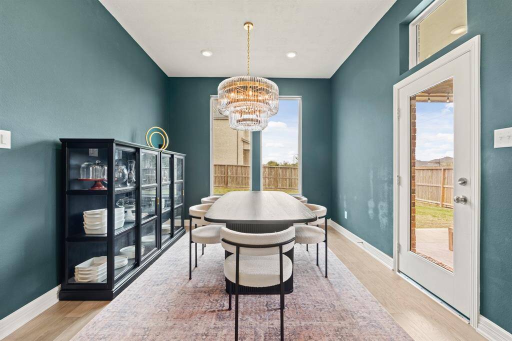 Sophisticated dining space with rich teal walls, dramatic windows, and a sparkling chandelier that adds warmth and elegance.