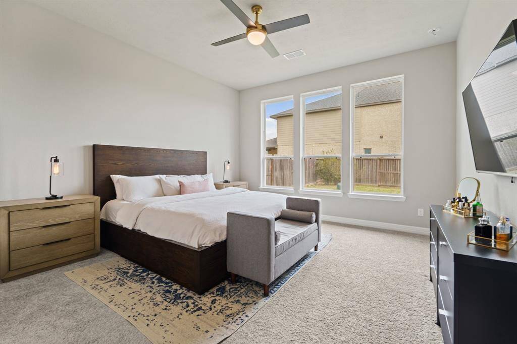 Spacious primary suite with soft carpeting, modern ceiling fan, and a wall of windows bringing in natural light.