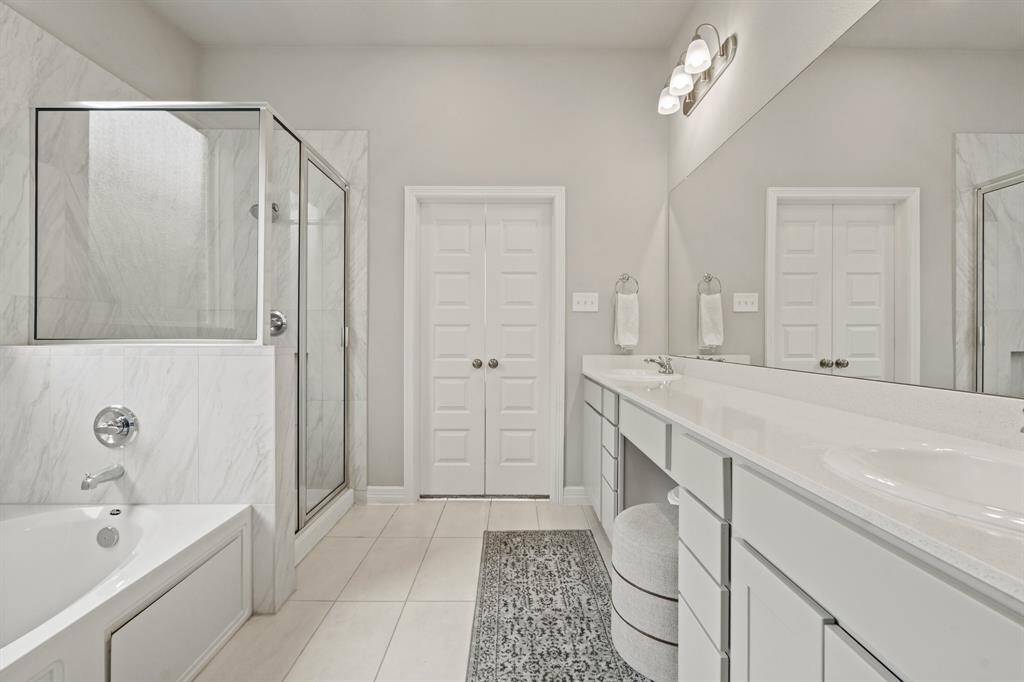 Luxury bathroom with dual vanities, soaking tub, walk-in shower, and plenty of storage behind elegant double doors.