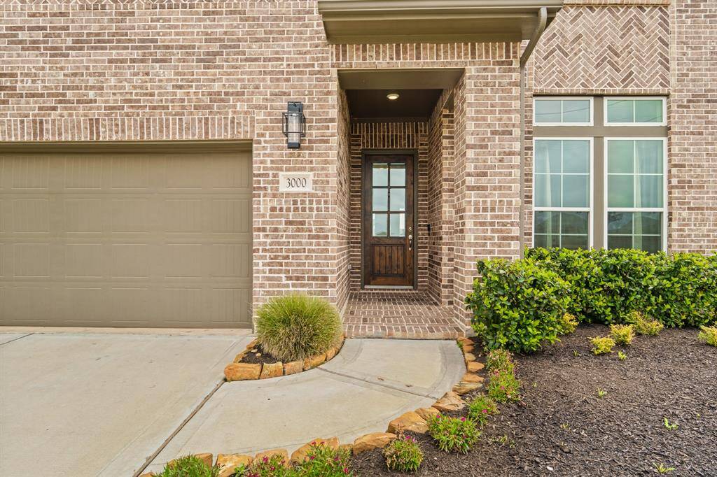 Charming entryway with a rich wood front door, brick accents, and well-kept landscaping that creates a warm and welcoming first impression.