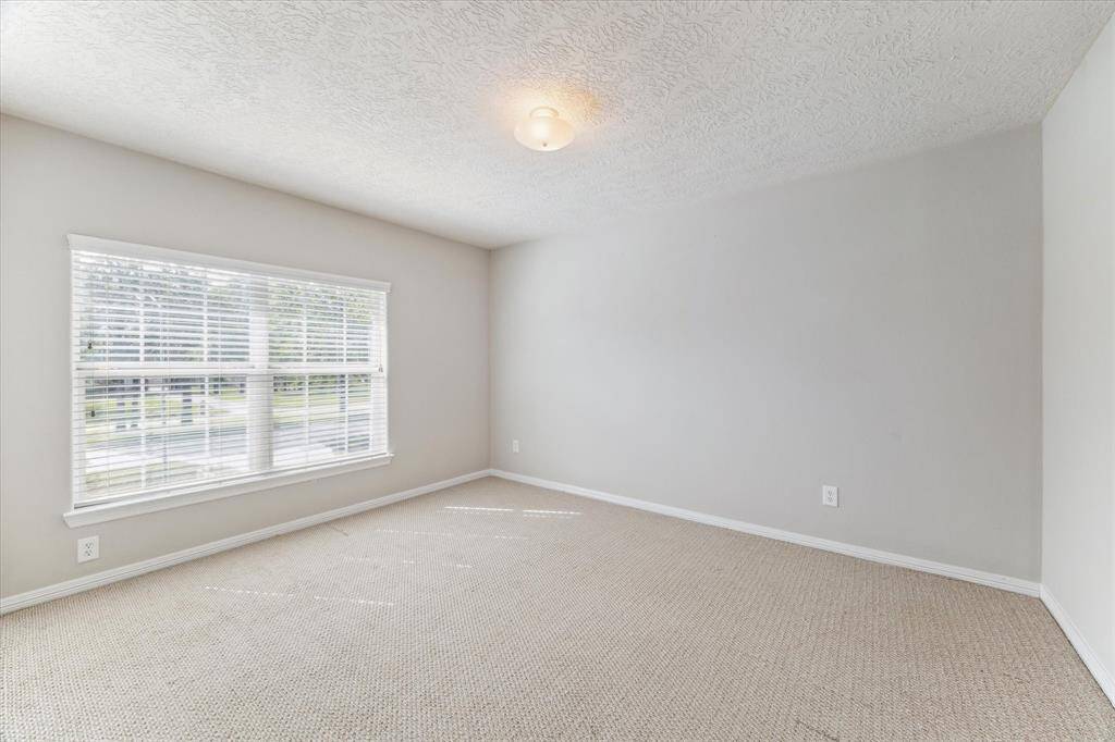 Another well-lit secondary bedroom featuring neutral walls, carpeted flooring, and views of the front yard.