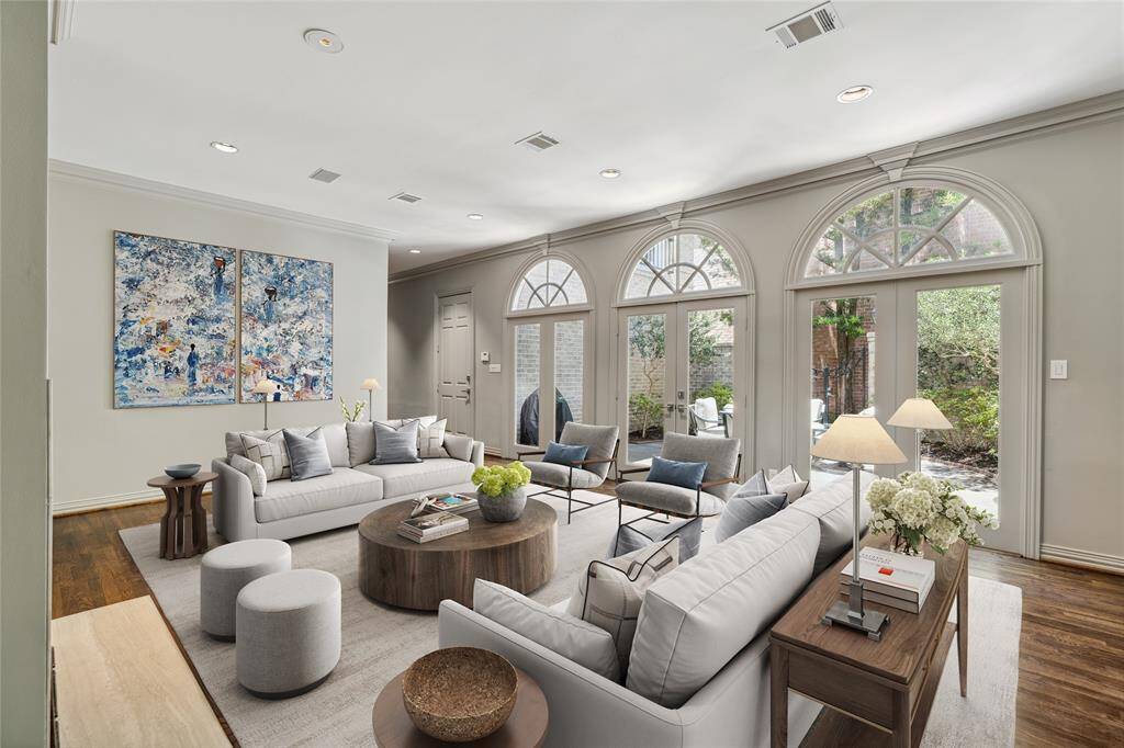 A view of the Family Room toward the double French doors.  The closed door is access to the attached 2-car garage.  Note the crown molding, recessed lighting and floor plugs (out of view).  The fireplace includes a marble hearth. This photo is virtually staged to show one possible configuration of furniture.