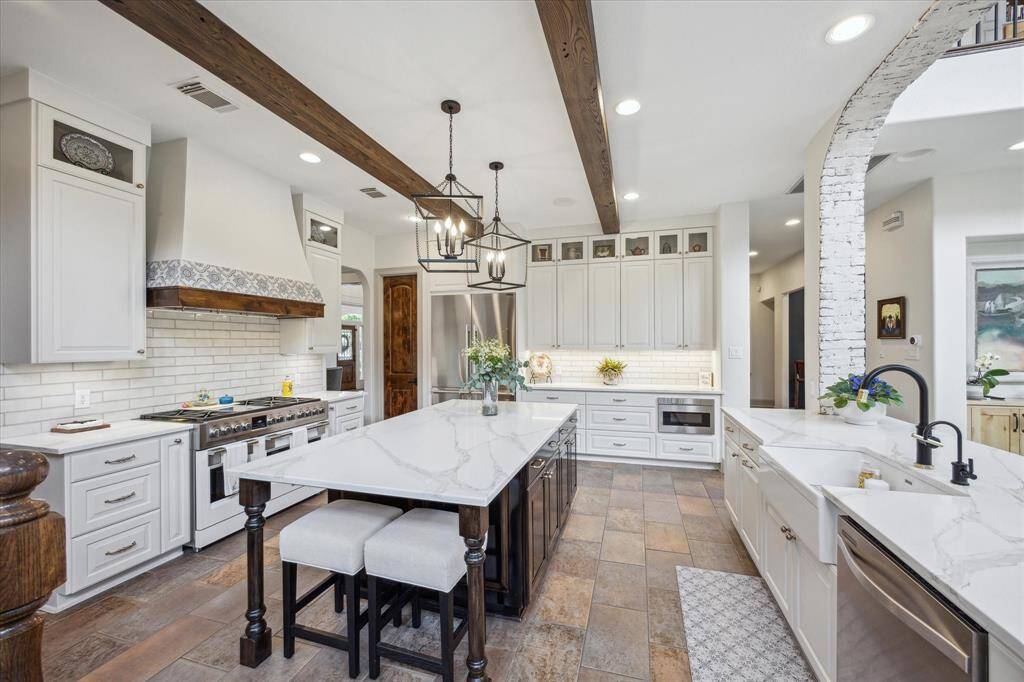 Another view of the expansive kitchen. Quartz countertops, custom built cabinetry, apron front sink, trash pull out with cutting board, water filter, walk in pantry, bricked arch opening with lime wash.