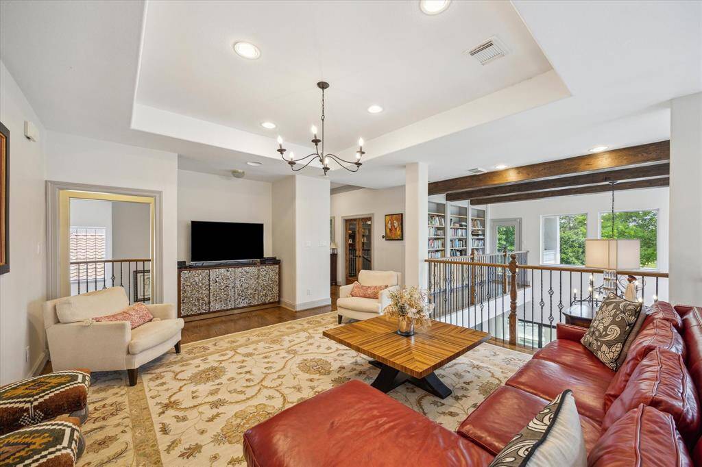 Second floor game room open to balcony overlook. Chandelier, wood flooring, bookshelves and access to exterior balcony.