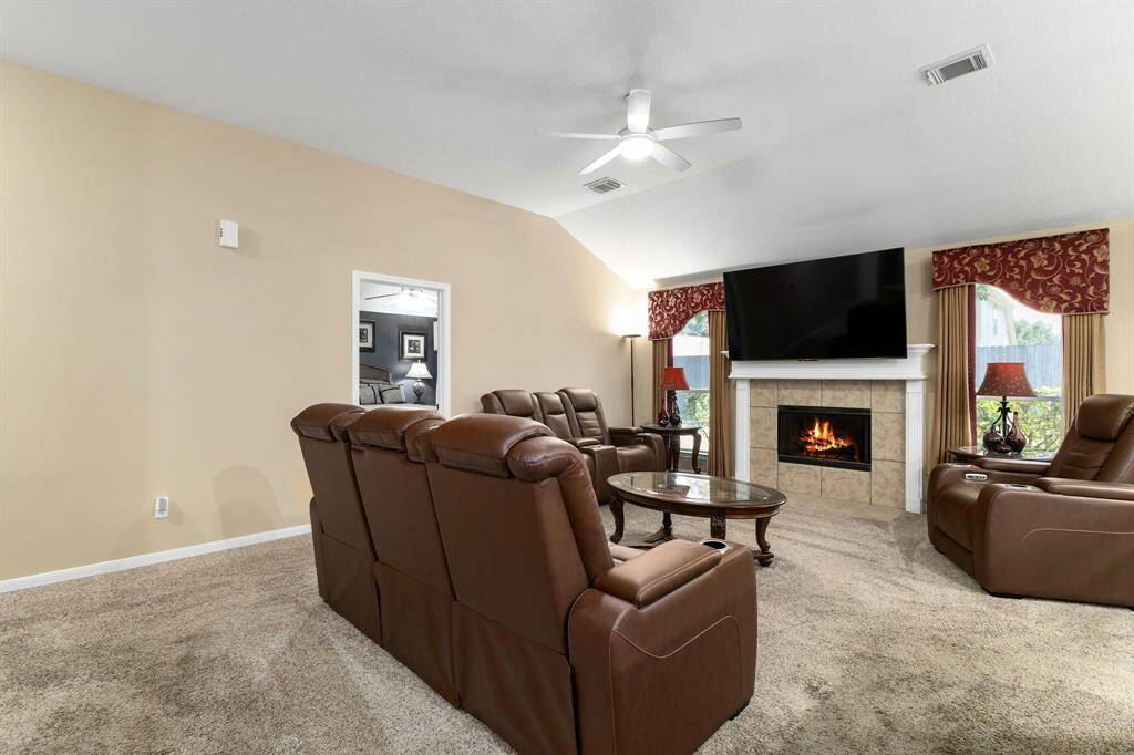 This spacious living room has a fireplace, a ceiling fan and natural light from the windows, creating a warm and inviting atmosphere.