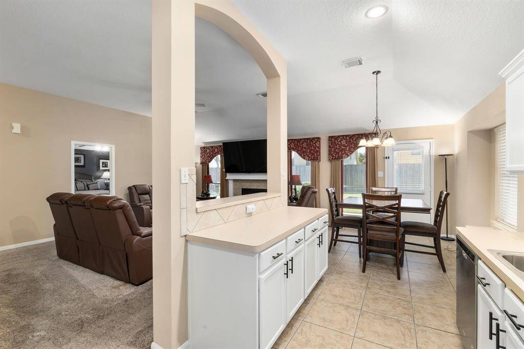 This open-concept living space features a kitchen with white cabinetry, a cozy dining area with ample natural light.  The neutral color palette enhances the airy feel, and large windows offer a view of the backyard.