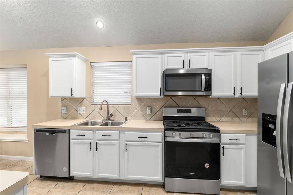 Modern kitchen featuring stainless steel appliances, including a gas stove and refrigerator. It has white cabinetry, a double sink, and a tiled backsplash, creating a bright and clean atmosphere.