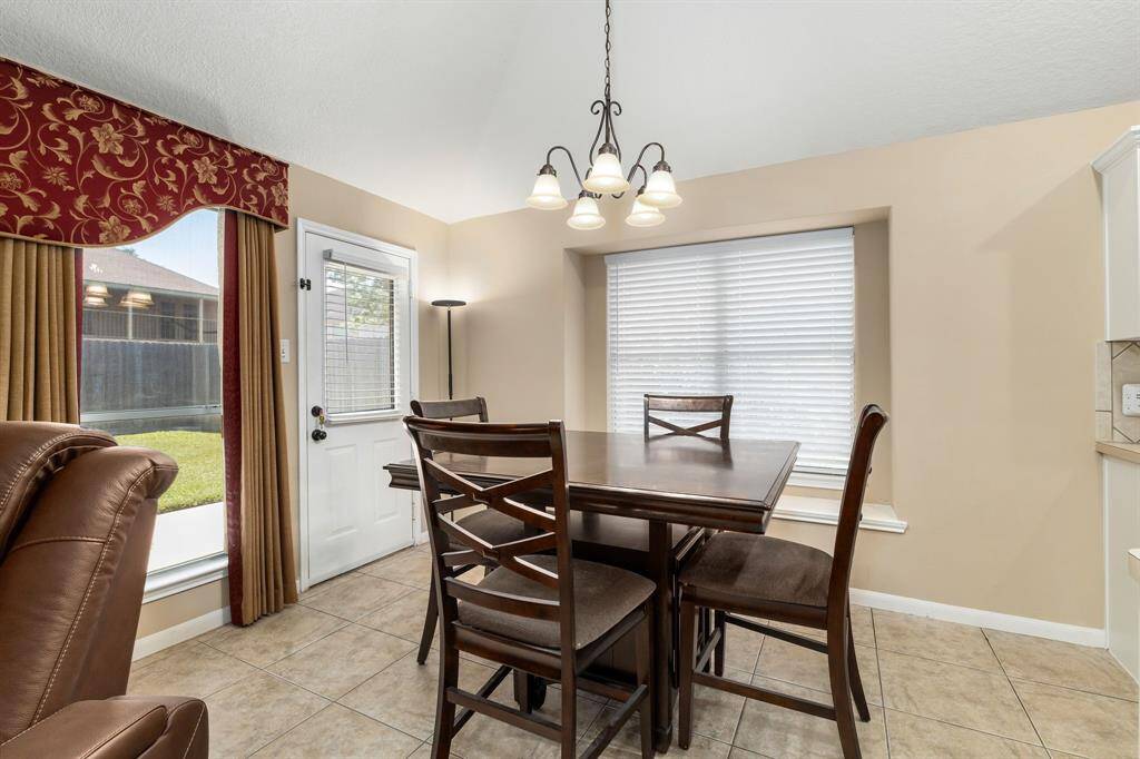 Bright dining area with tiled floors.  It has large windows with blinds and curtains, offering a view of the backyard. A glass door leads outside, and a stylish light fixture enhances the cozy atmosphere.
