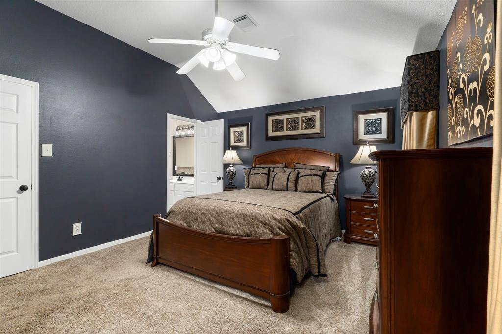 Primary bedroom with vaulted ceiling, dark accent walls, plush carpet, walk-in closet, and ensuite bath.