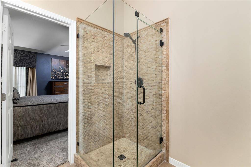 This photo showcases a modern, glass-enclosed shower with elegant stone tile walls and flooring.