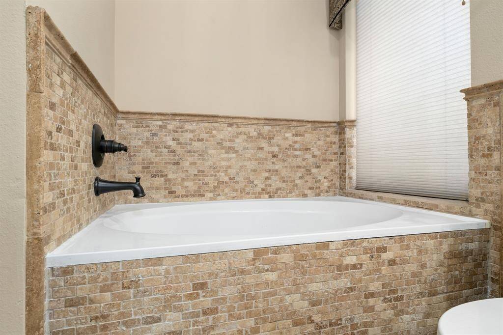 This bathroom features a soaker tub with elegant stone tile surround and black fixtures, offering a cozy and stylish space for relaxation.