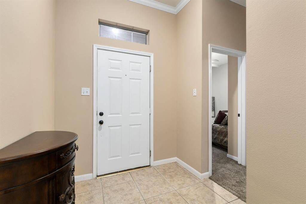 This photo shows a welcoming entryway with a white door, beige walls, and tiled flooring.