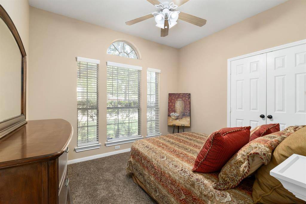 Guest bedroom features a large arched window that provides ample natural light, neutral walls, and a ceiling fan.