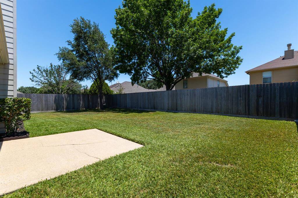 Lush green landscaped yard with a concrete patio area, fully fenced for privacy—ideal for relaxing or entertaining outdoors.
