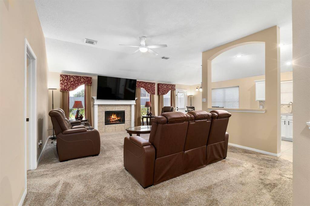 This cozy living room features plush carpeting, a gas woodburning fireplace and archway leading to the kitchen. Natural light fills the space, creating a warm and inviting atmosphere.