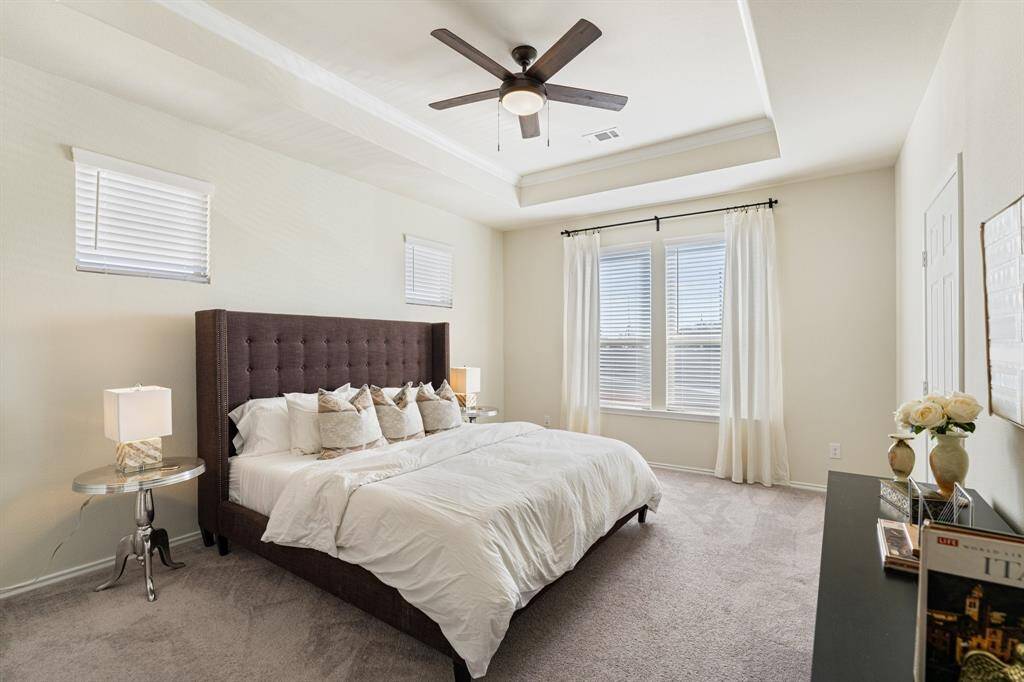 Spacious master bedroom features a raised ceiling and ceiling fan and abundant natural light. En suite bathroom includes a double vanity, large walk-in shower, private lavatory, and dual large walk-in closets.