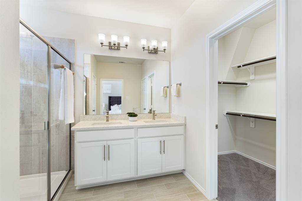 View of primary bathroom including roomy walk-in shower, dual sinks, water closet, and generous storage space.