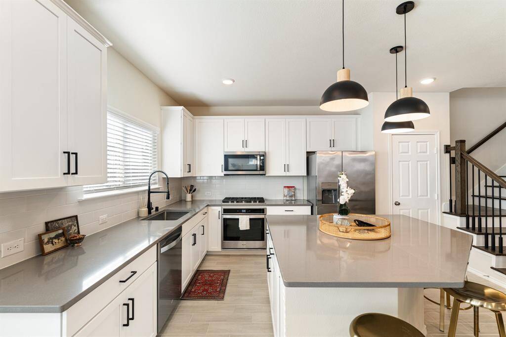 Kitchen features stainless steel Whirlpool appliances, beautiful quartz countertops, shaker style cabinetry with sleek black hardware, and a sturdy stainless steel sink with a pull-down faucet. In addition to the abundant cabinet space, there is plenty of storage in the pantry, complete with built-in shelves.