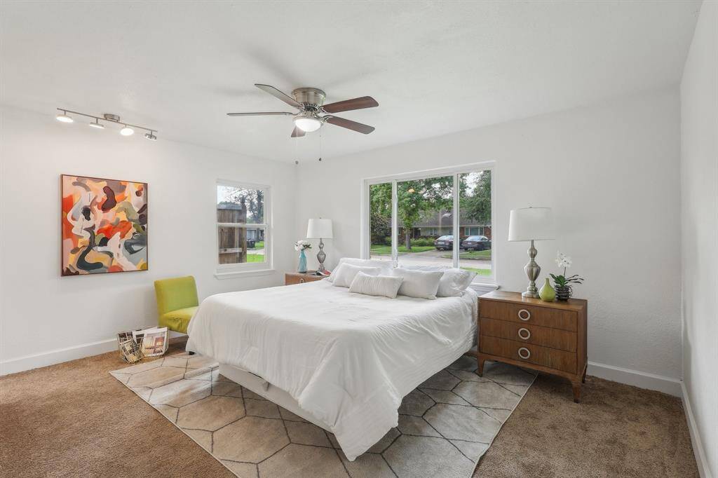 This bright and airy bedroom features a large window with a view, neutral carpet, and white walls.