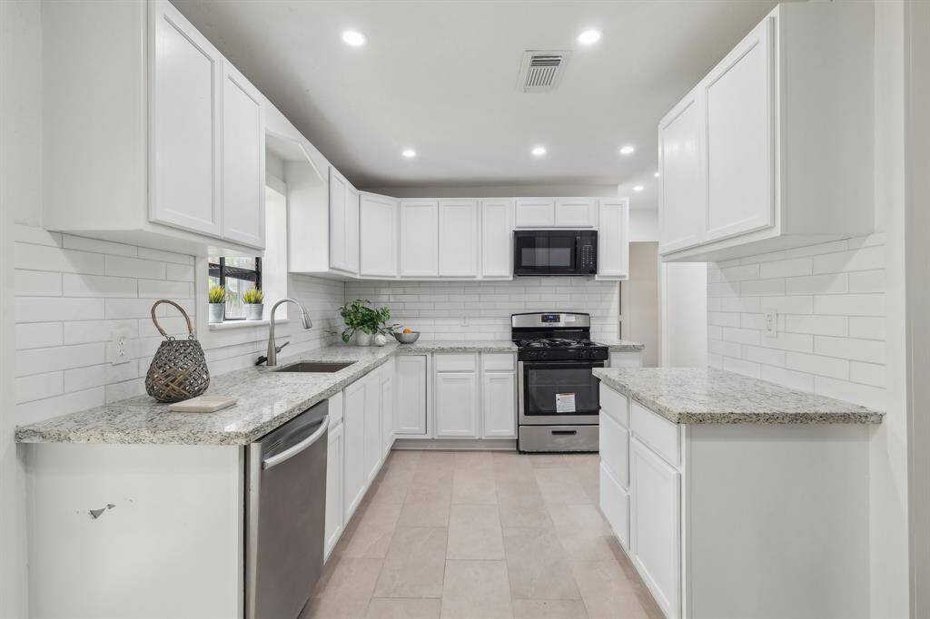 This modern kitchen features sleek white cabinetry, granite countertops, and stainless steel appliances, including a dishwasher and oven. The bright space is complemented by a subway tile backsplash and recessed lighting, offering a clean and inviting atmosphere.