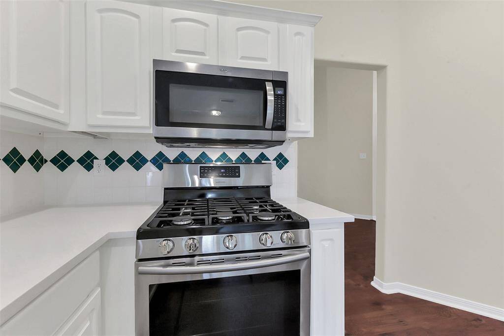 Modern kitchen with stainless steel gas stove and microwave, white cabinetry, and a stylish tile backsplash featuring diamond patterns.
