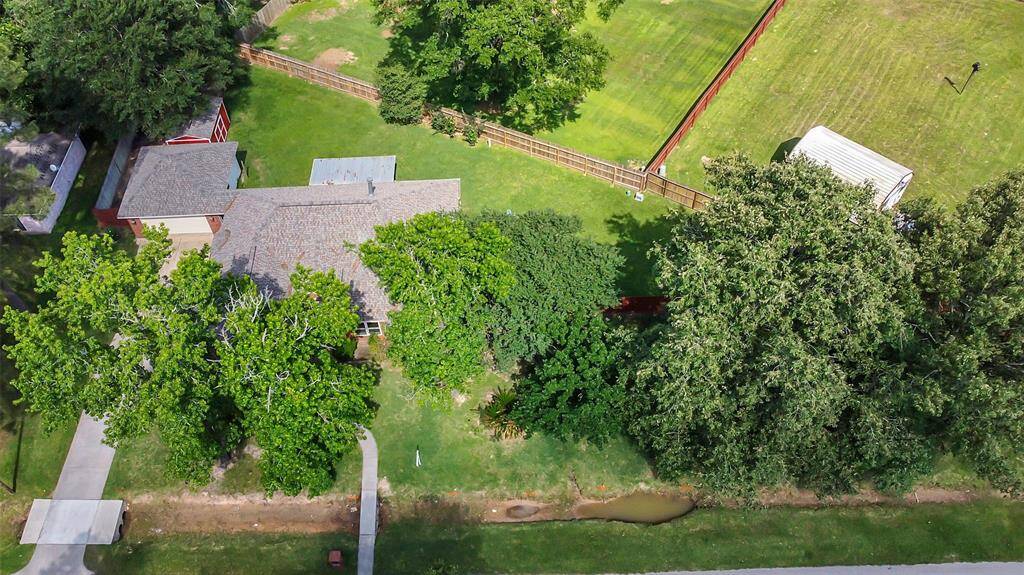 This aerial view shows a single-story home surrounded by lush greenery and mature trees. The property includes a spacious backyard with a fenced area and a separate structure or shed. It offers ample privacy and a peaceful setting, perfect for outdoor activities or gardening.