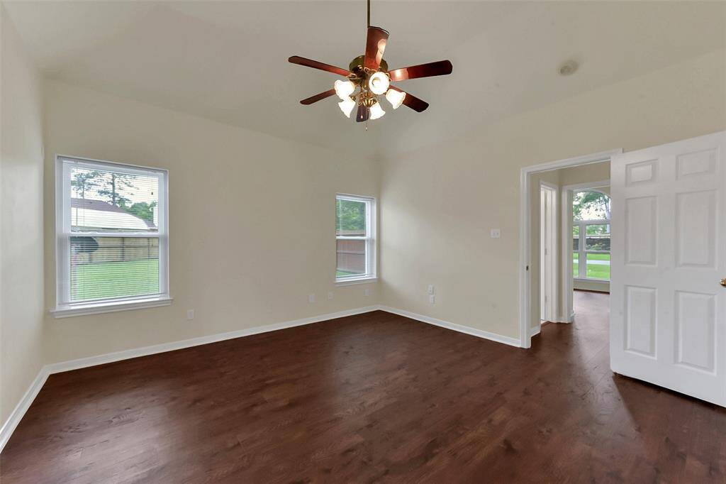 Spacious room with hardwood floors, neutral walls, and a ceiling fan. It features two windows for natural light and an open doorway leading to another room.