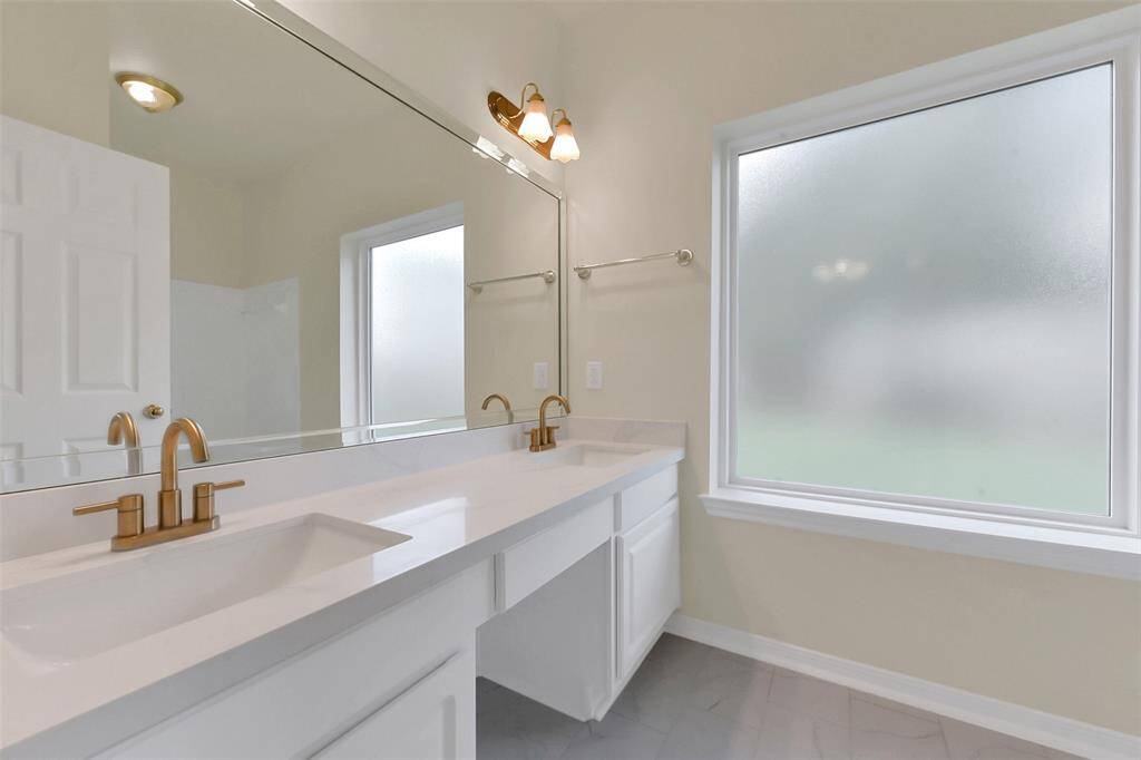 Bright and modern bathroom with a large double vanity, sleek fixtures, and frosted window for privacy.