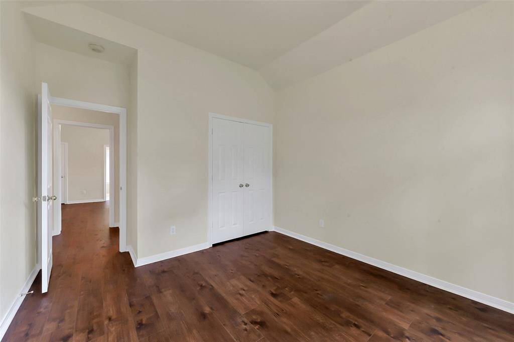 This room features hardwood flooring, neutral-colored walls, and a closet with double doors. It opens to a hallway with a view of another room, offering a spacious and connected layout.