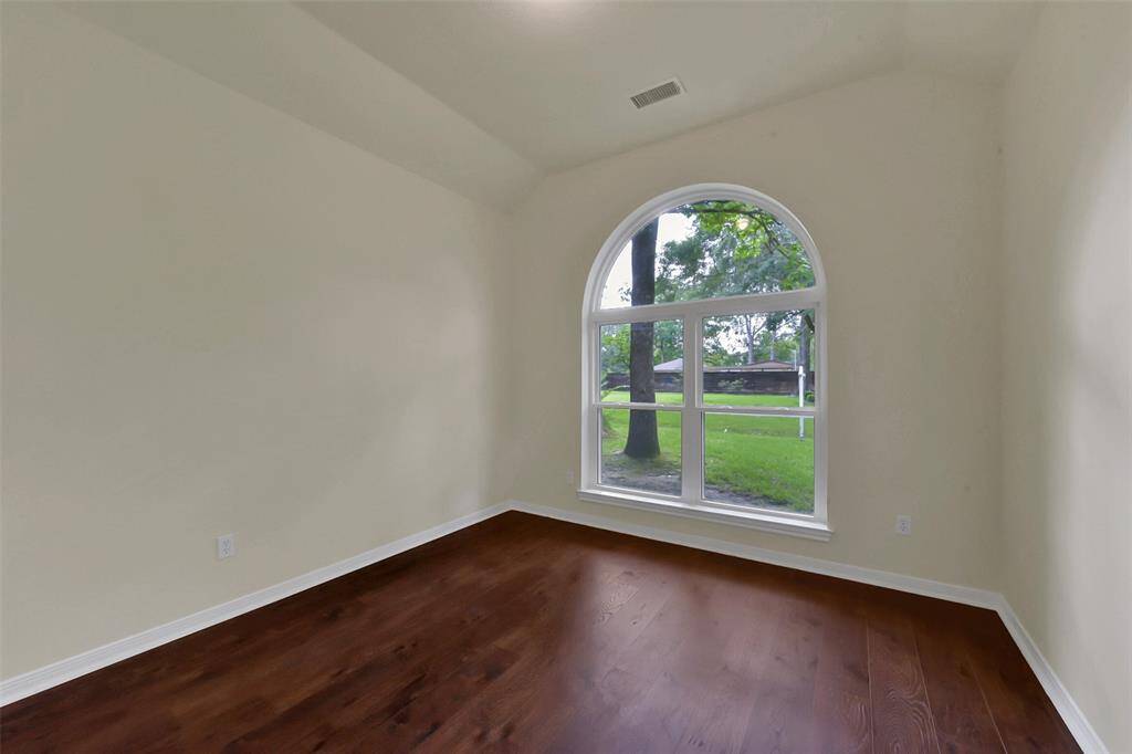 This room features a large arched window providing plenty of natural light and a view of the greenery outside. It has hardwood floors and neutral-colored walls, creating a bright and inviting space.