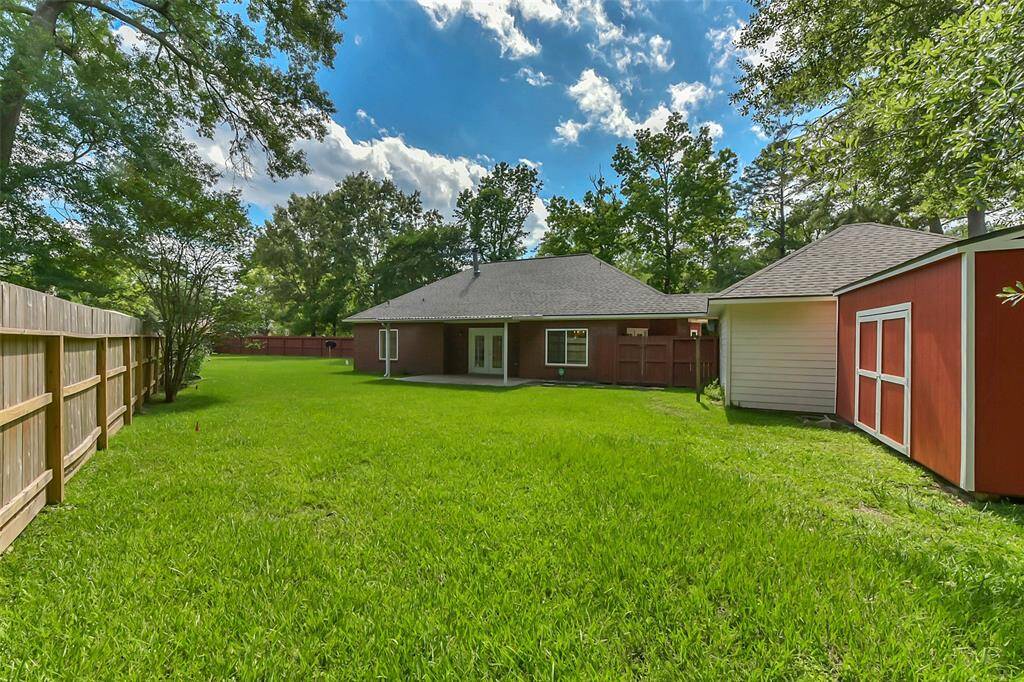 This photo shows a spacious backyard with a well-maintained lawn, fenced on one side. The house features a large patio and a separate red outbuilding, surrounded by mature trees for added privacy.
