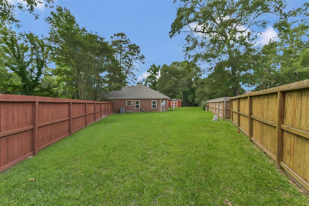 Spacious backyard with a well-maintained lawn, bordered by wooden fences and surrounded by mature trees, offering privacy and a serene atmosphere. Ideal for outdoor activities and relaxation.