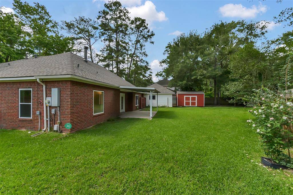 Charming brick home with a spacious backyard, featuring a covered patio and a red storage shed. Surrounded by mature trees, offering privacy and a serene atmosphere.