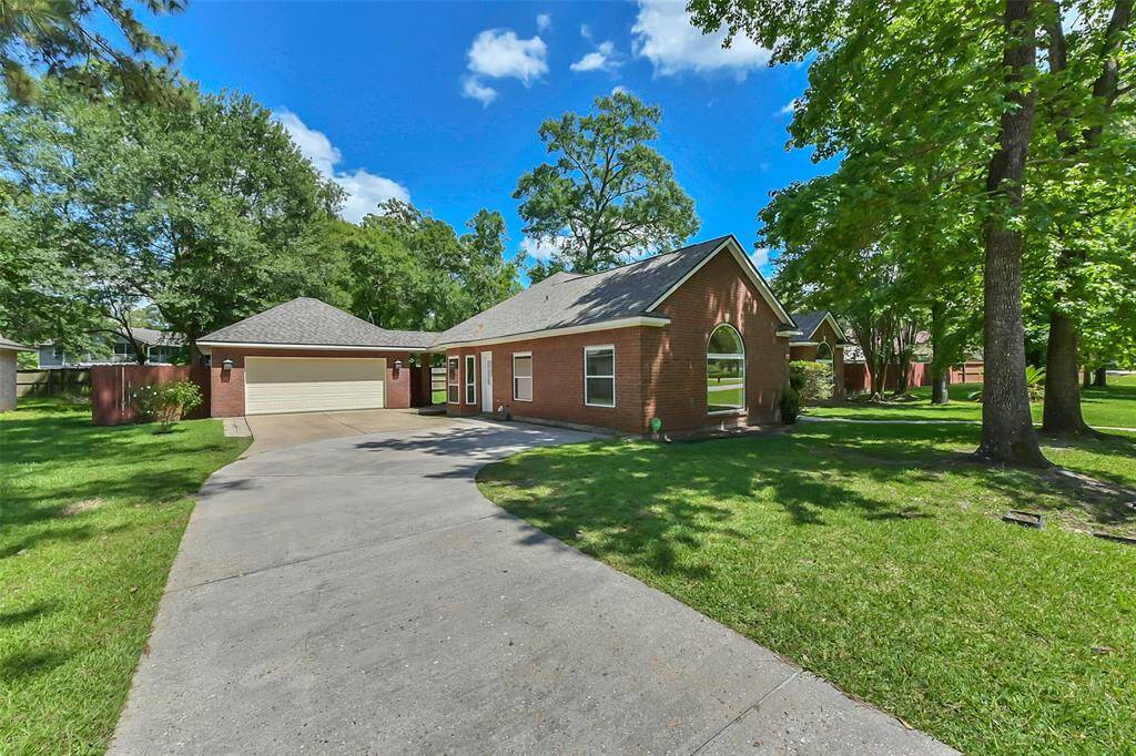 This charming brick home features a two-car garage and a spacious driveway. It's surrounded by lush green trees and a well-maintained lawn, offering a serene and inviting atmosphere.