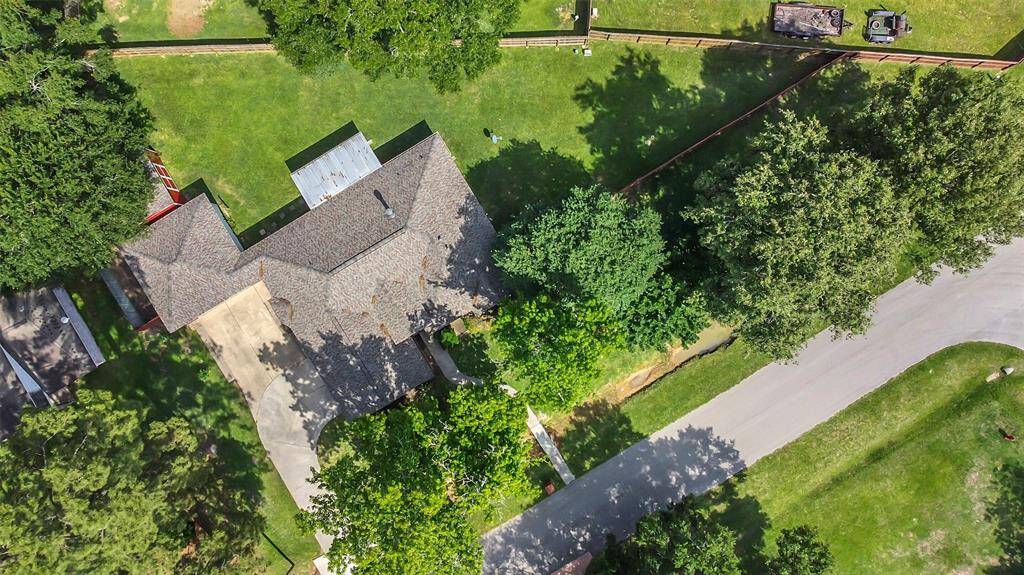 This aerial view showcases a spacious home with a large yard, surrounded by mature trees for privacy. The property features a long driveway and is situated on a quiet street, offering a serene and secluded setting.