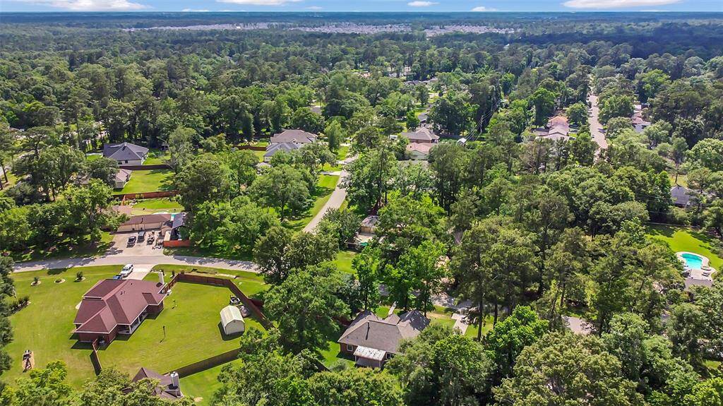 This aerial photo showcases a peaceful, tree-lined residential neighborhood with spacious properties, ample greenery, and a mix of modern homes. The area appears to offer privacy and a suburban feel, ideal for families or those seeking tranquility.