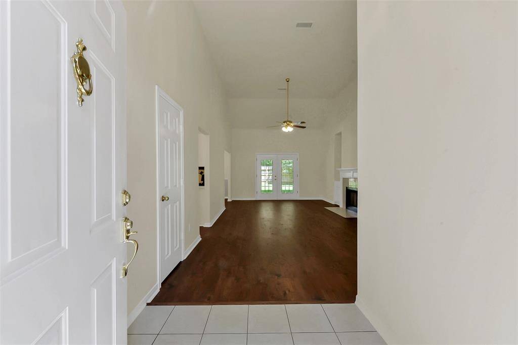 This photo shows a spacious entryway leading into a living area with high ceilings and wood floors. There's a ceiling fan, a fireplace, and glass doors that offer a view of the backyard.