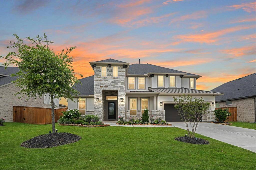 This is a beautiful two-story home with a modern stone and stucco exterior, a well-maintained lawn, and a two-car garage. It features a welcoming front porch and attractive landscaping, set against a picturesque sunset sky.