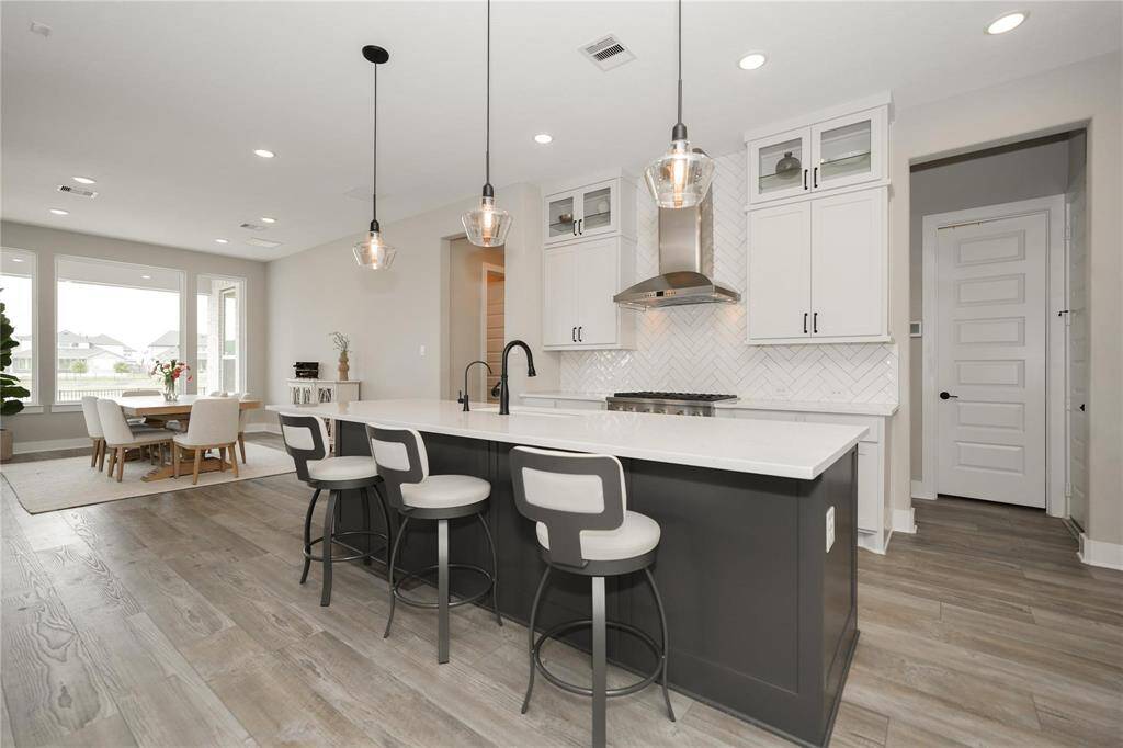 This photo showcases a modern kitchen with an open layout, featuring a large island with seating, sleek white cabinets, and stainless steel appliances. The space is bright and airy, with a dining area that has ample natural light from large windows, and stylish pendant lighting enhancing the contemporary feel.