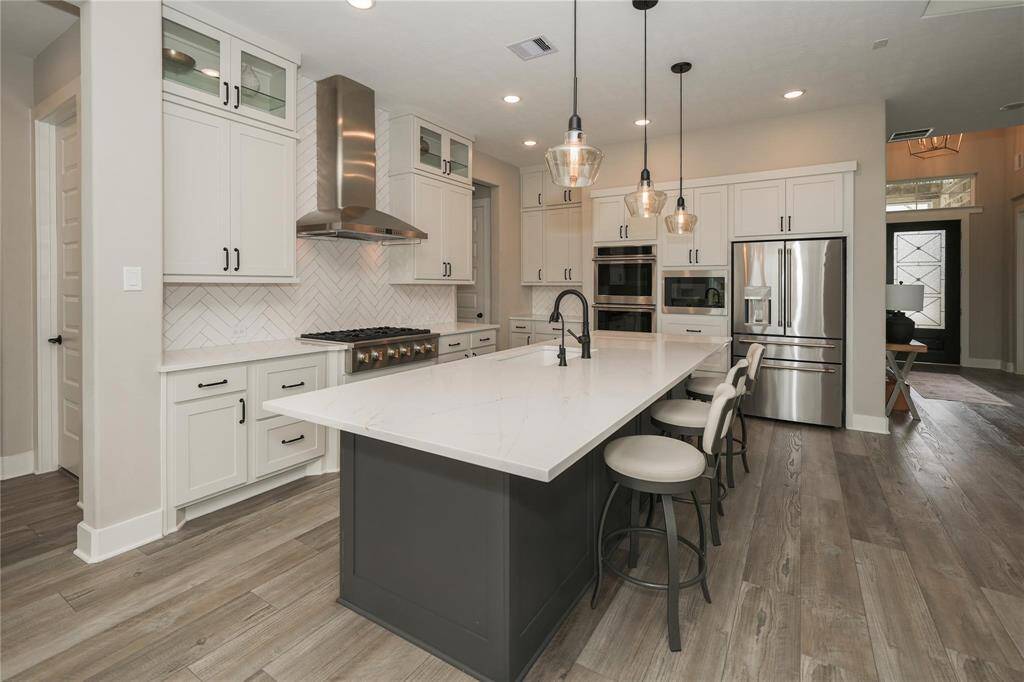 This modern kitchen features a spacious island with seating, sleek stainless steel appliances, and elegant cabinetry. The pendant lighting and wood flooring add warmth, while the large fridge and double ovens offer convenience. Perfect for entertaining and everyday cooking.
