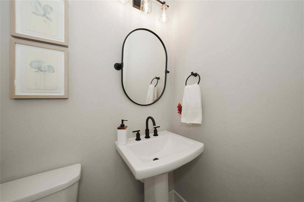 Cozy, modern half-bathroom with a sleek pedestal sink, black fixtures, an oval mirror, and minimalistic decor. Perfect for guests.
