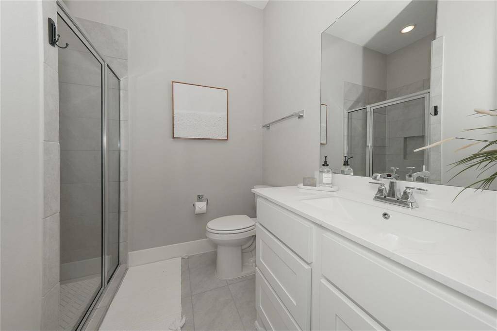 This bathroom features a modern design with a glass-enclosed shower, a sleek double vanity with ample storage, and neutral tile flooring. The space is bright and well-lit, offering a clean and contemporary feel.
